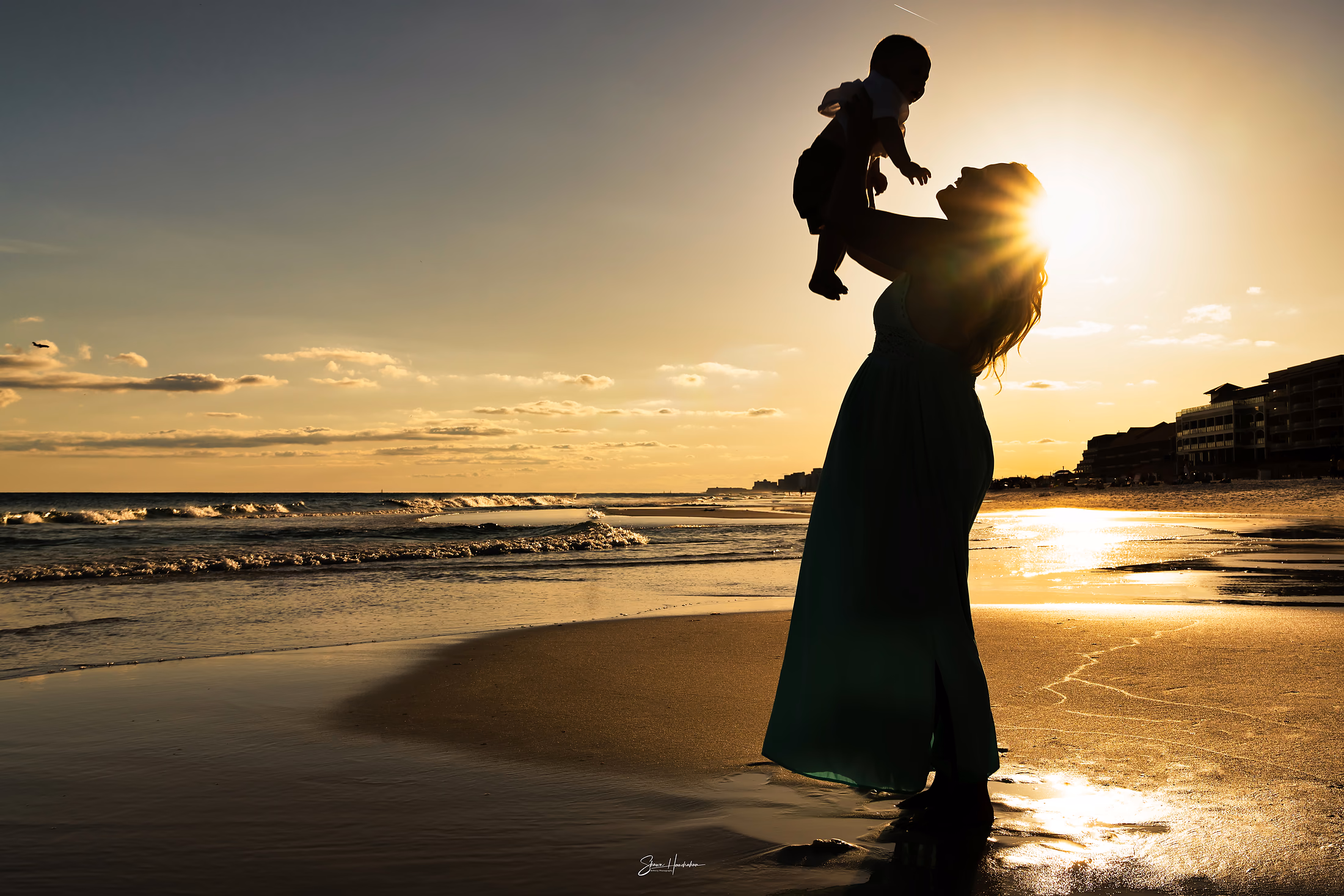 Parent lifting a small child against the sunset on the beach