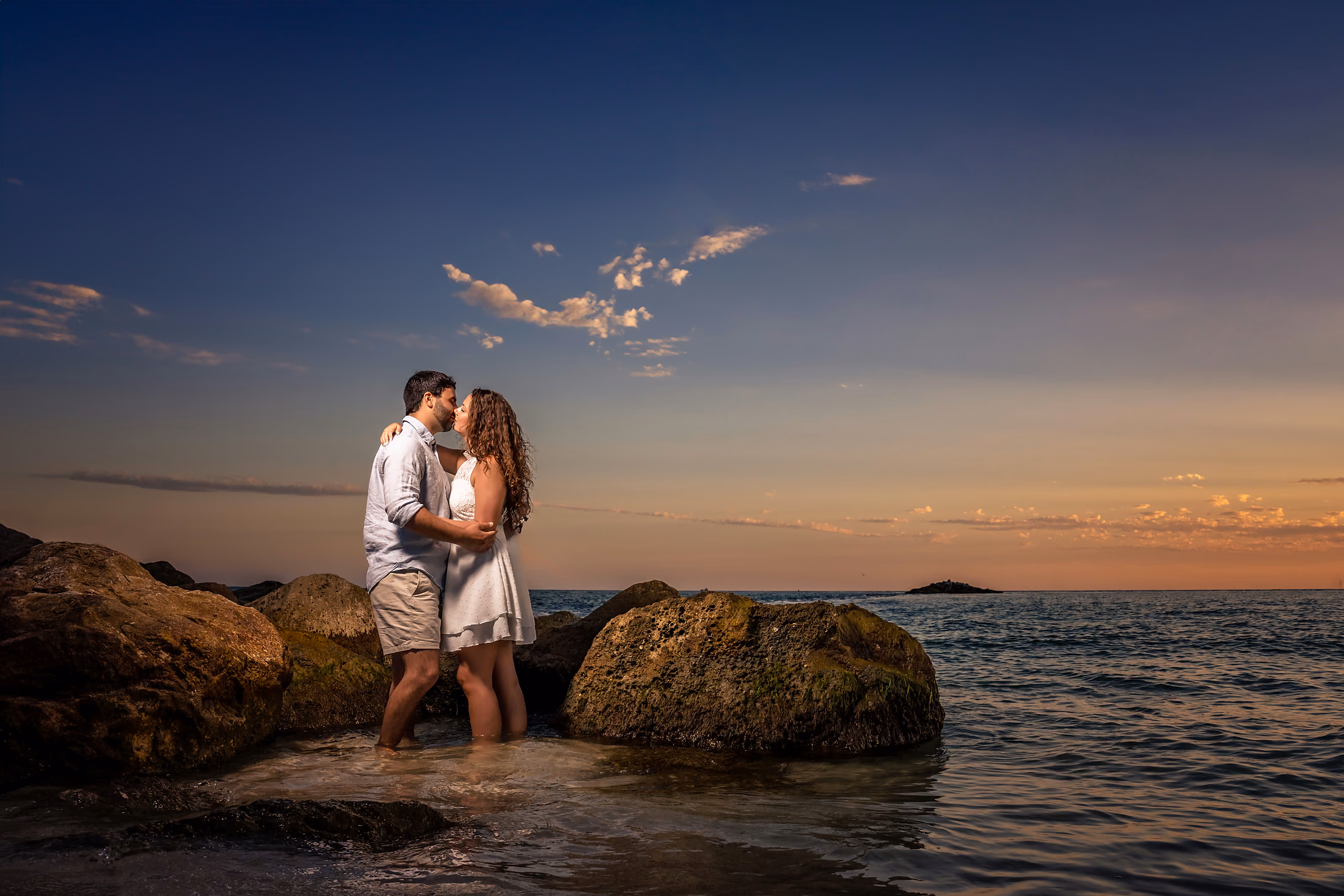 Couple embracing on the rocks as the sun sets over the water