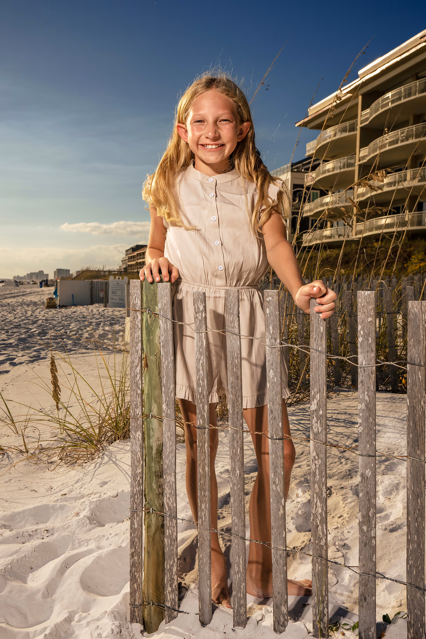 Young girl smiling beside a weathered beach fence