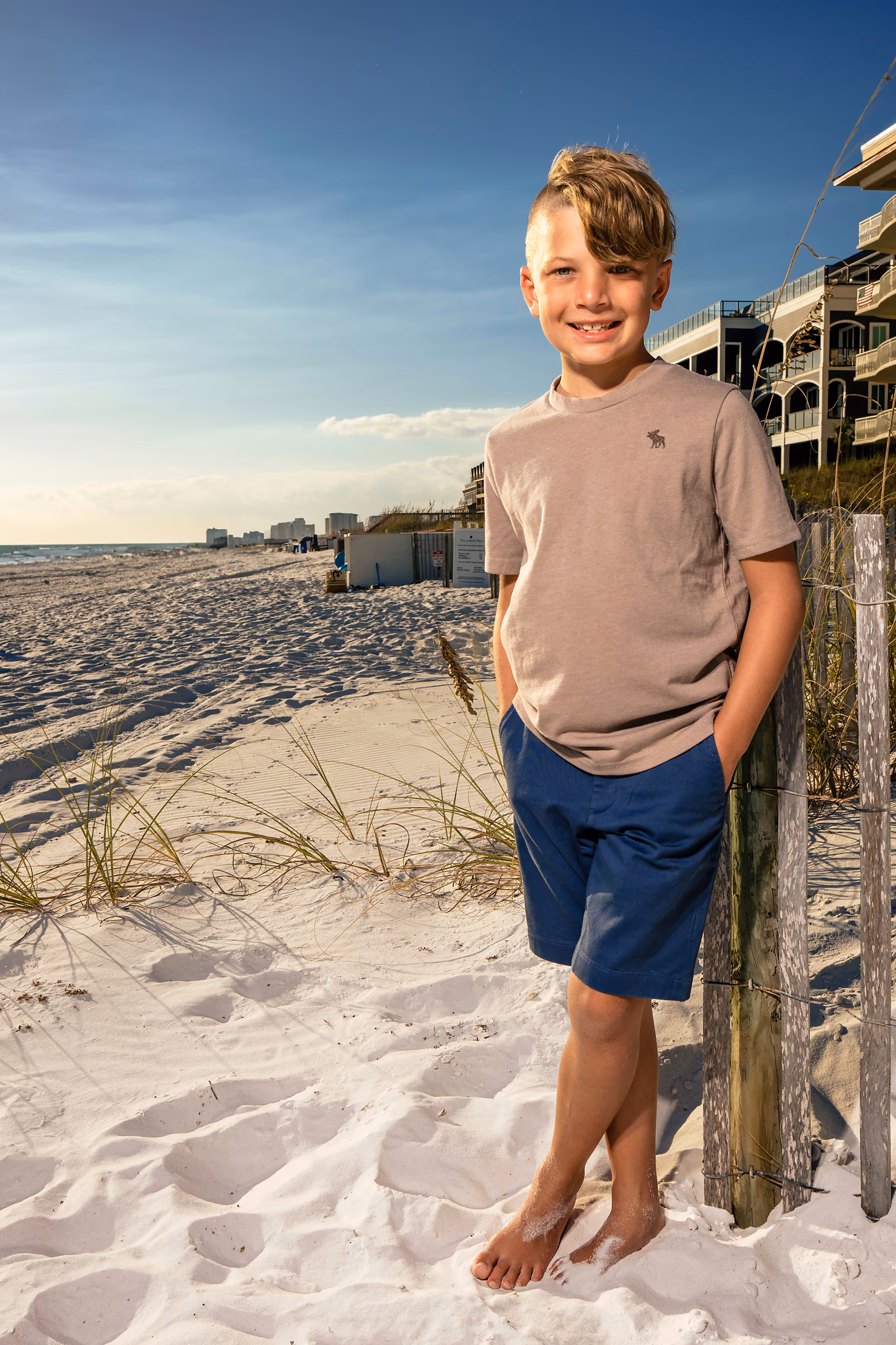 Young boy standing on the beach by the dune fence