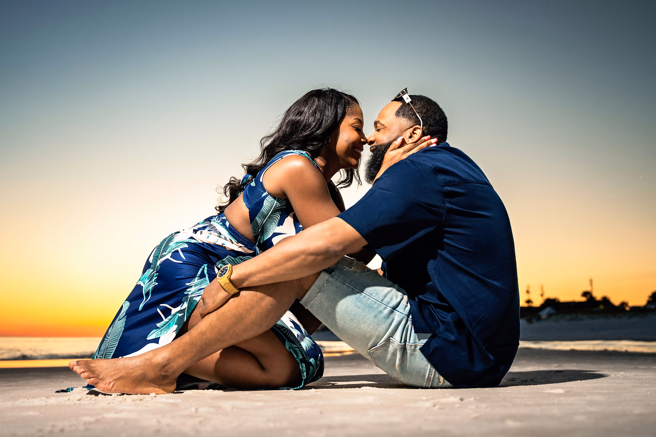 Couple sitting close on the sand, foreheads touching at sunset