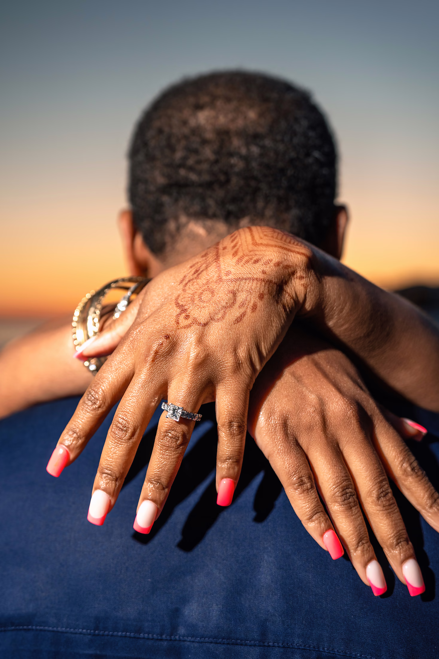 Close-up of a bride's hands, rings showing, around her partner's neck