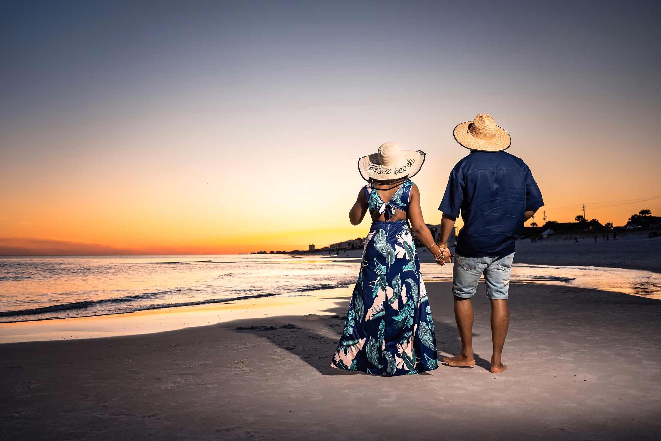 Couple in hats strolling the shoreline at sunset