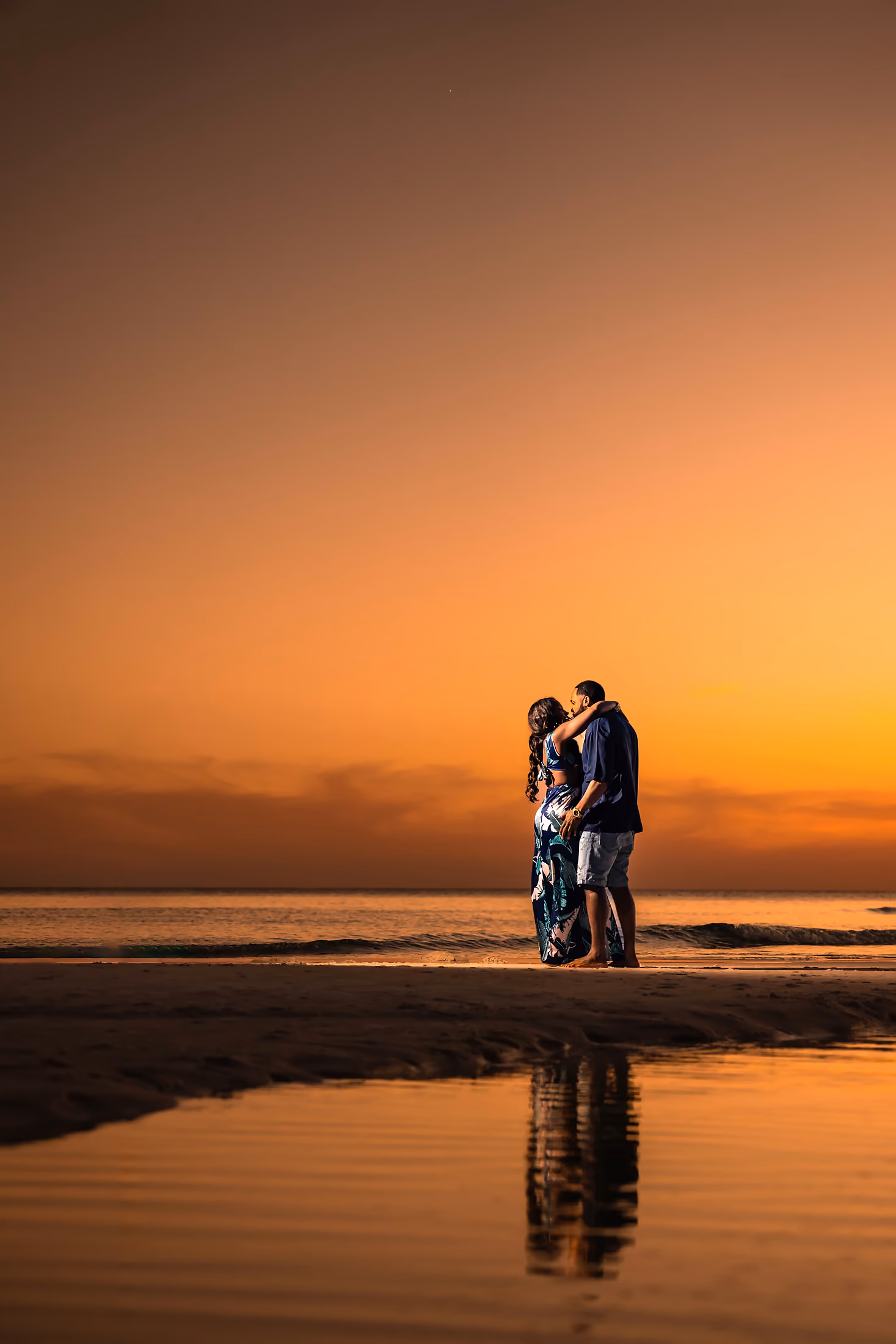 Couple reflected on the wet sand beneath a wide sunset sky