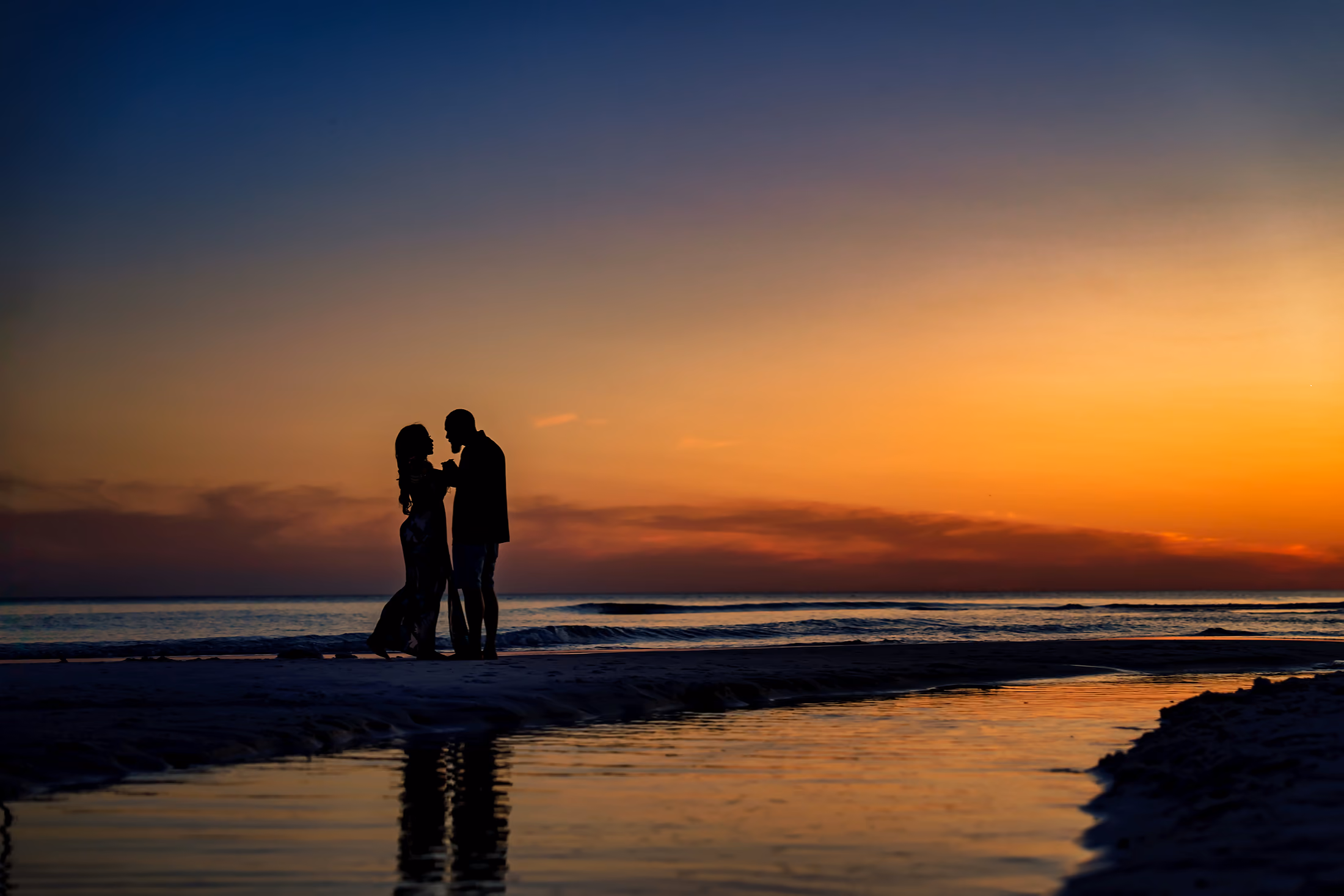 Couple silhouetted on a sandbar between sky and water