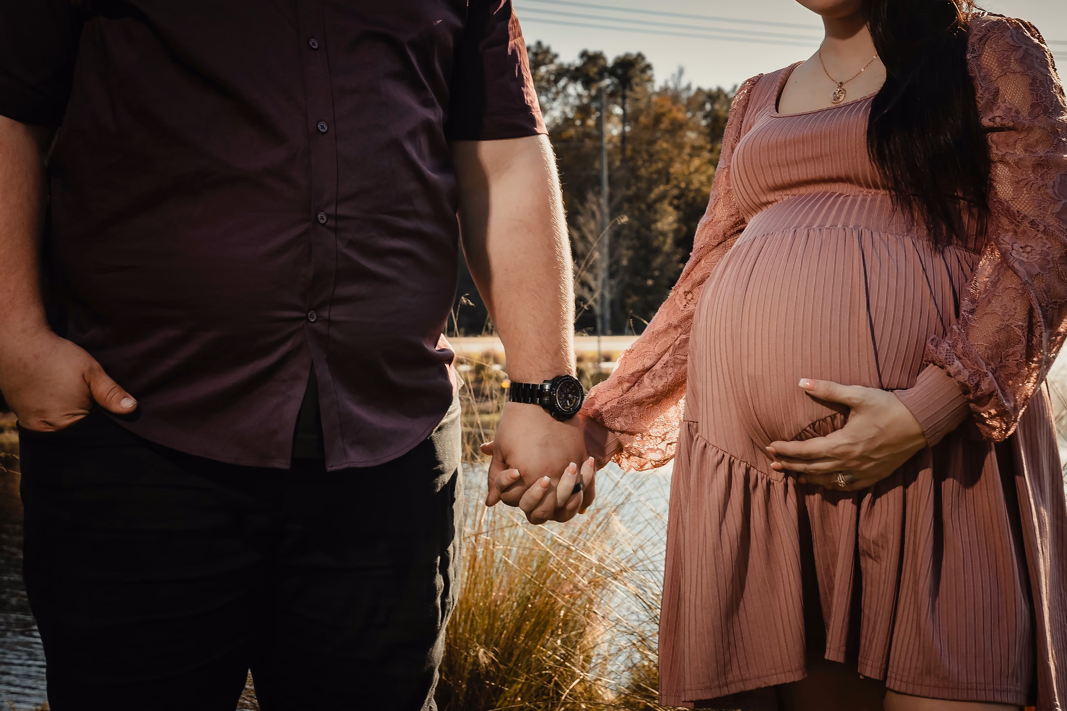 Expecting parents' hands resting on the bump in the dunes