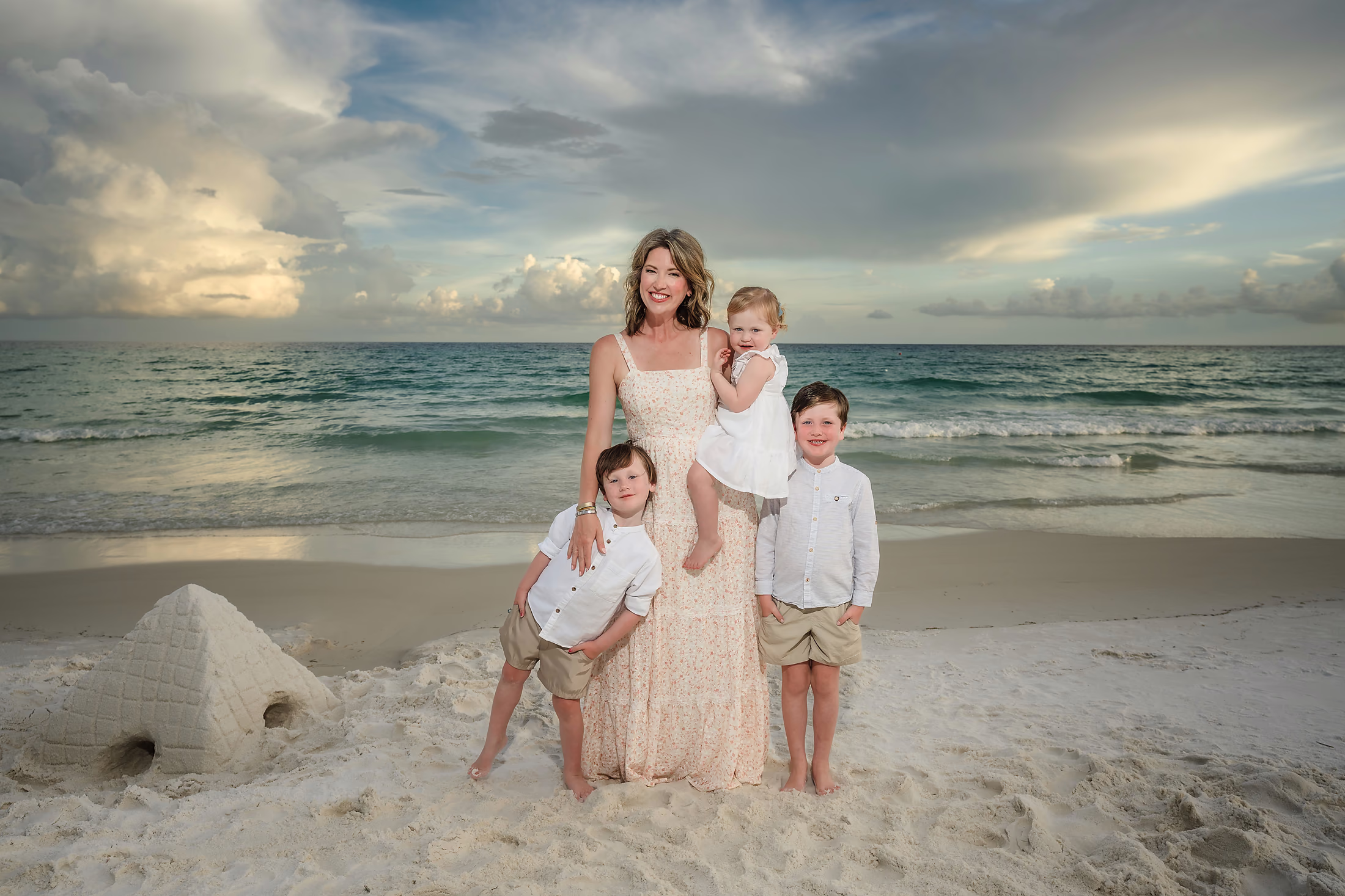 Mother and children beside a sandcastle at sunset