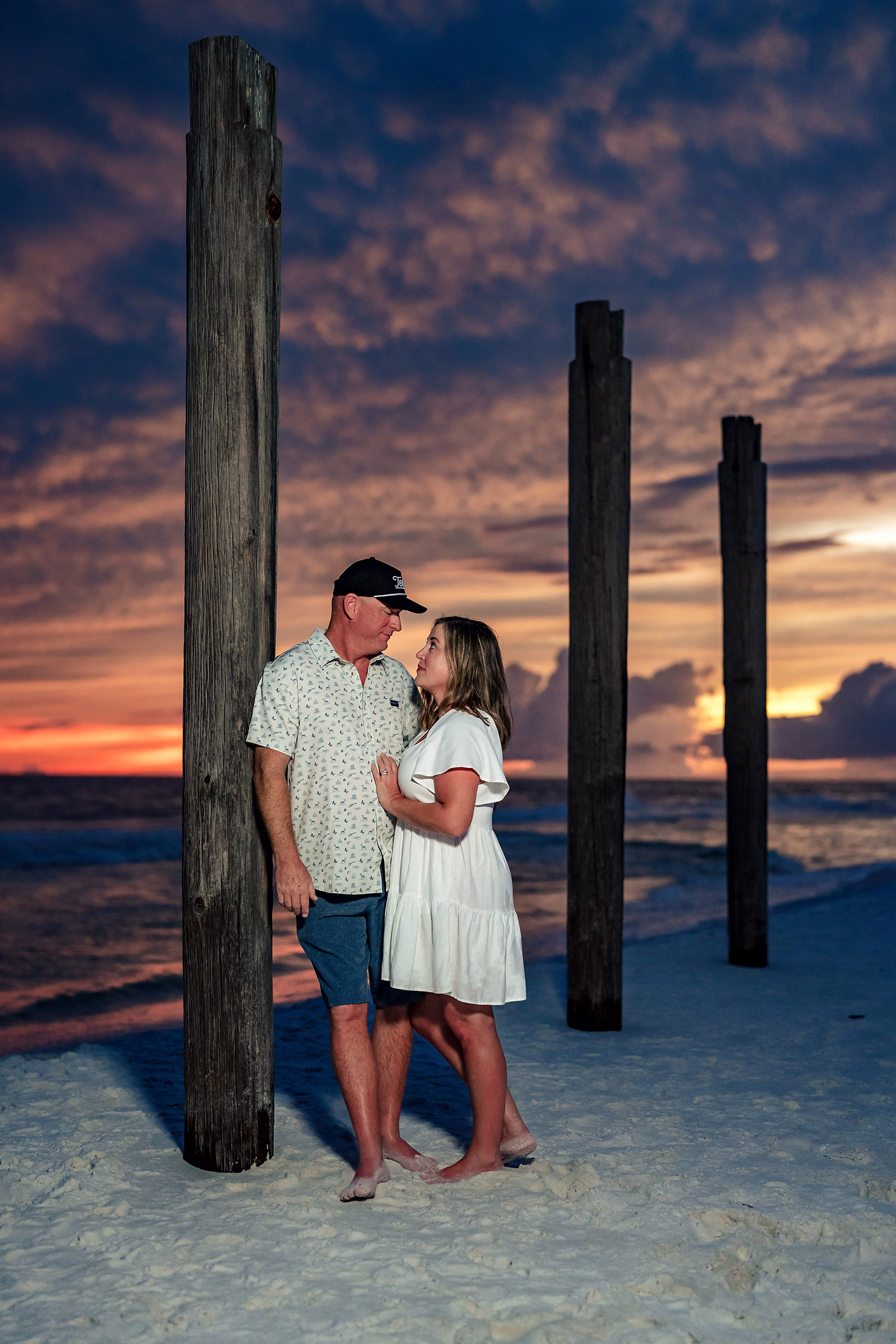Couple framed by weathered pier pilings at sunset