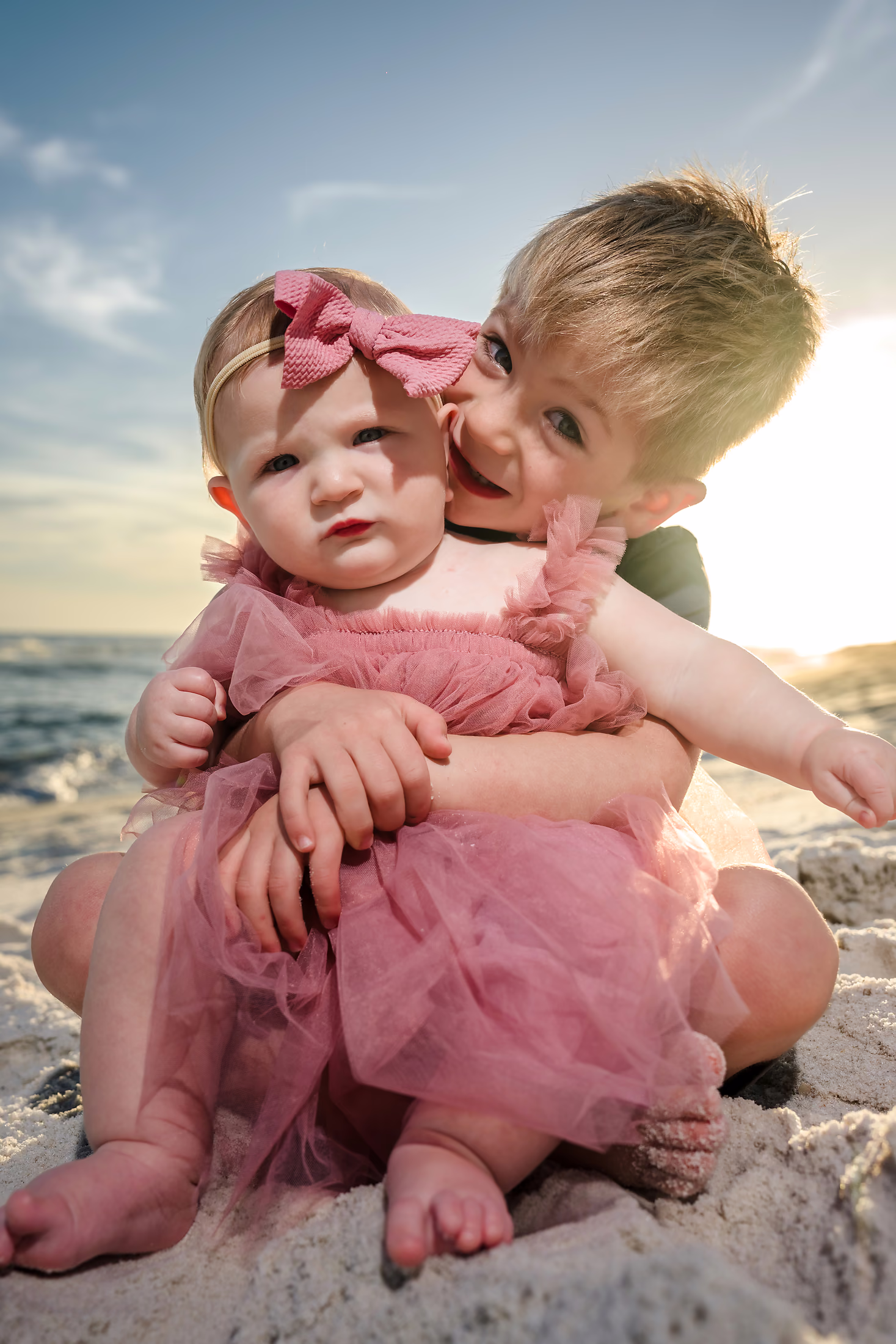 Big brother kissing his baby sister on the beach at sunset