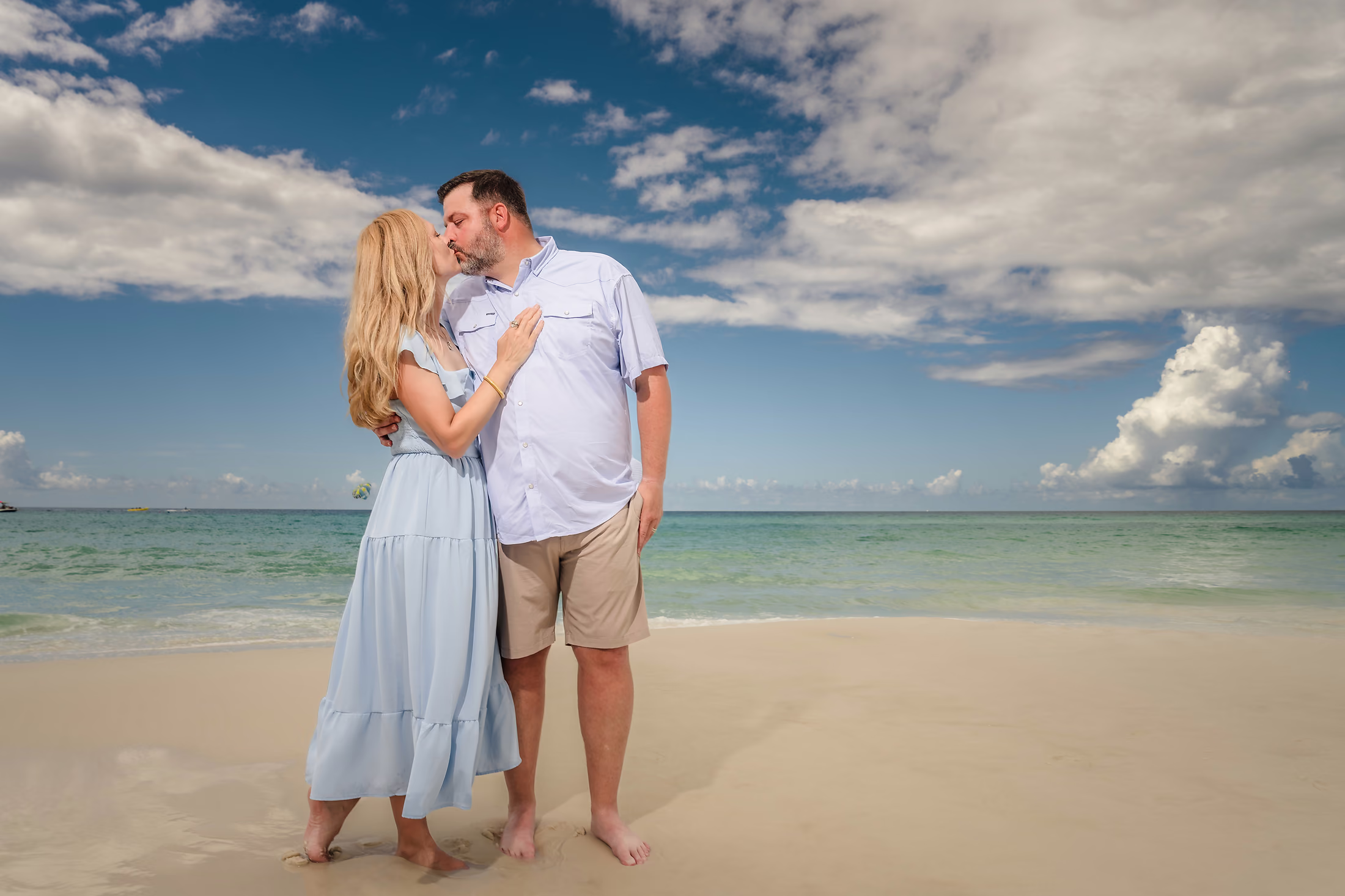 Couple embracing on the beach beneath a bright blue sky