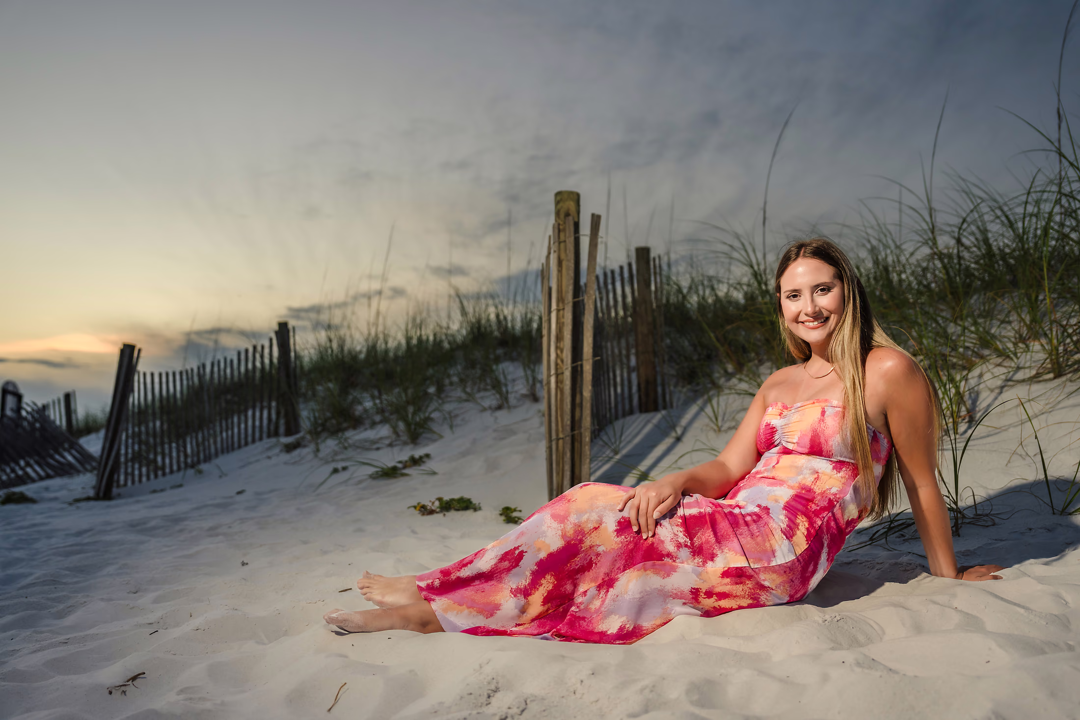 Woman in a magenta dress seated in the dunes at sunset