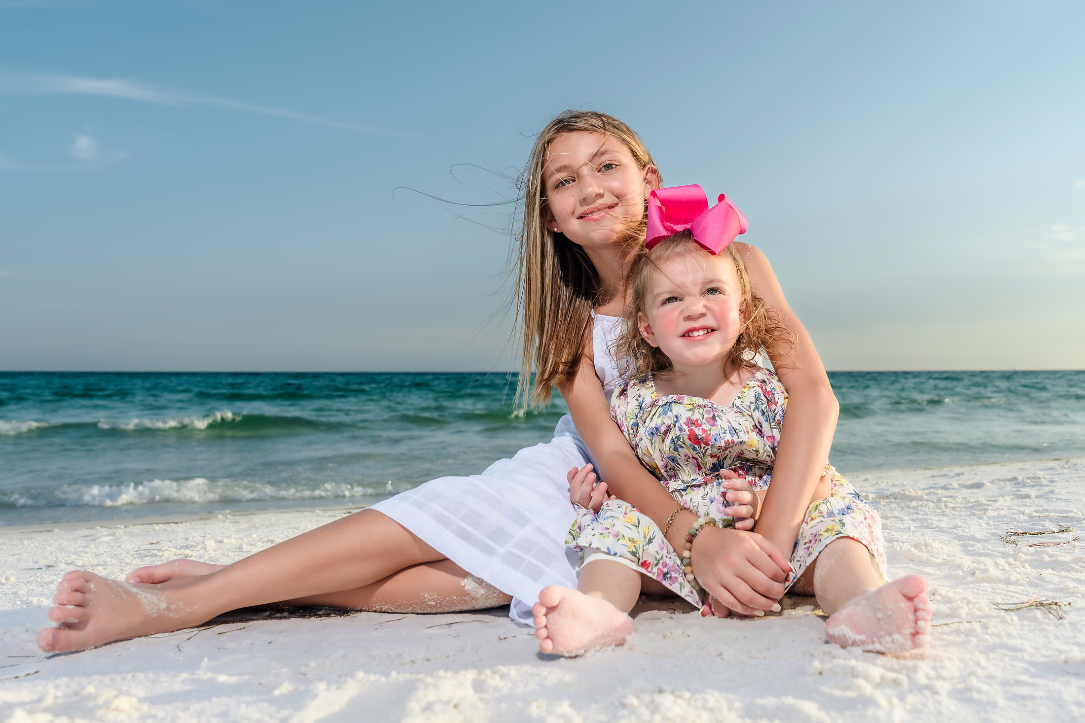 Two sisters hugging on the beach above clear water
