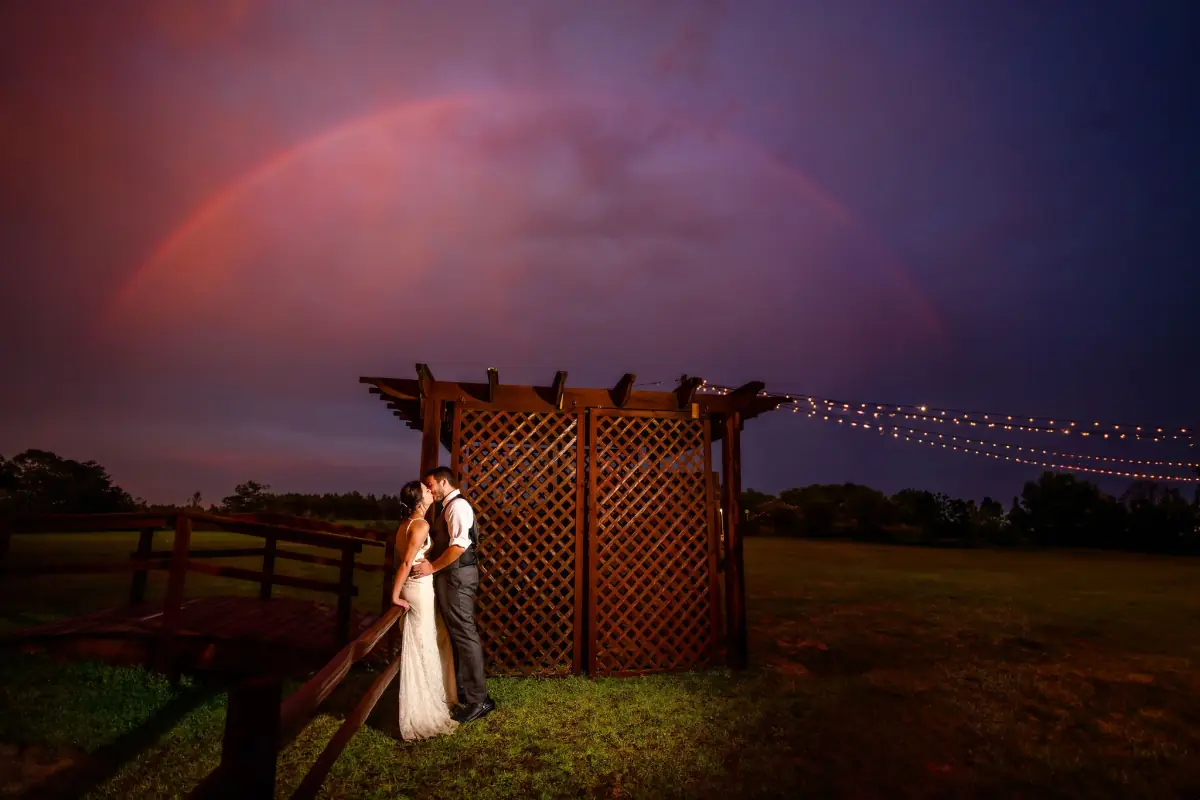 Bride under a passing rainbow by the rustic fence at Sowell Farms
