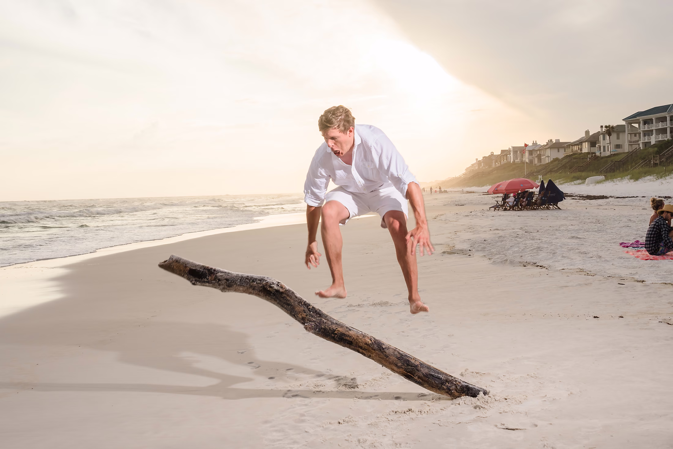Groom seated on a driftwood log at sunset