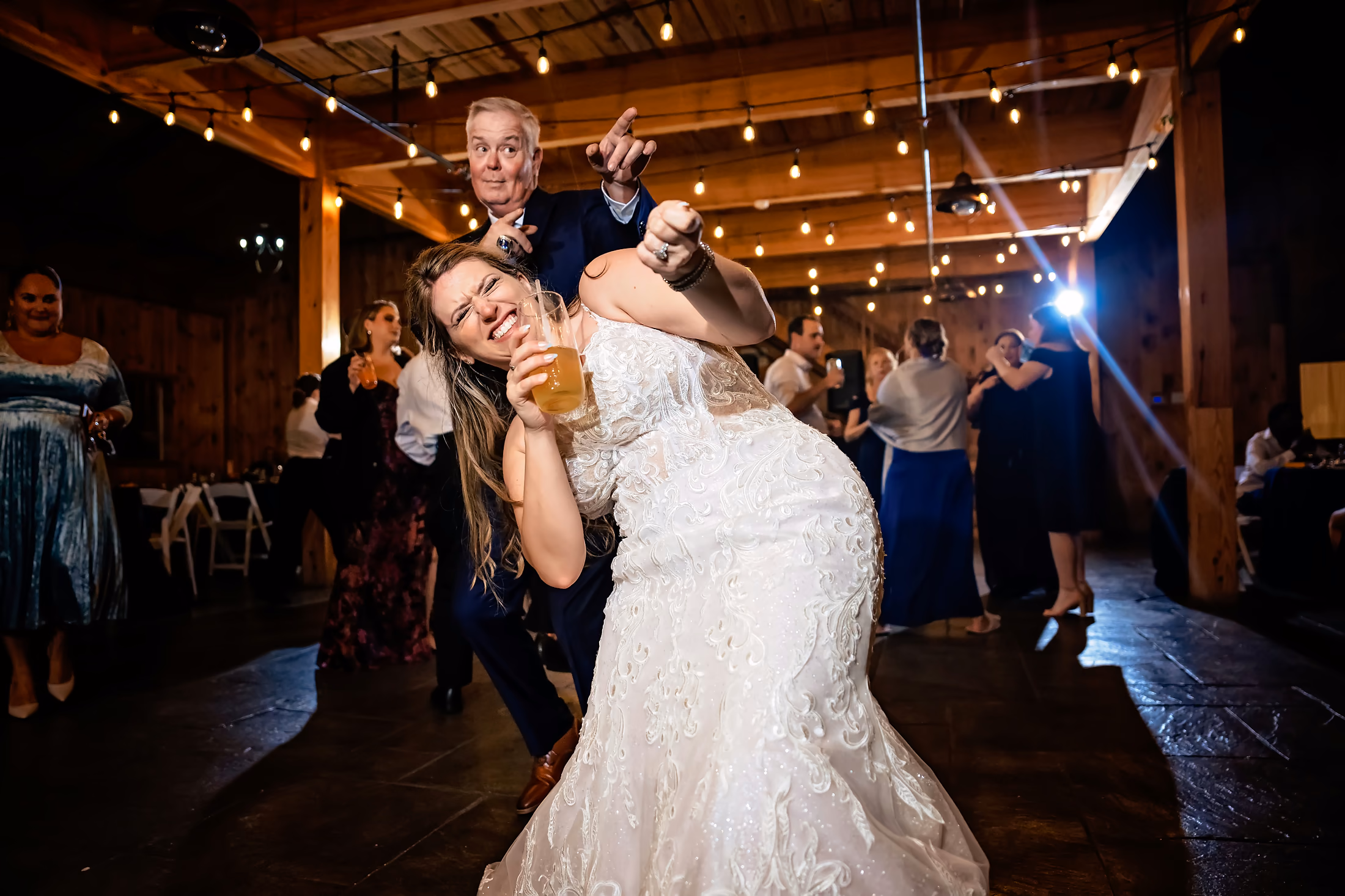 Bride and groom laughing on the dance floor under string lights