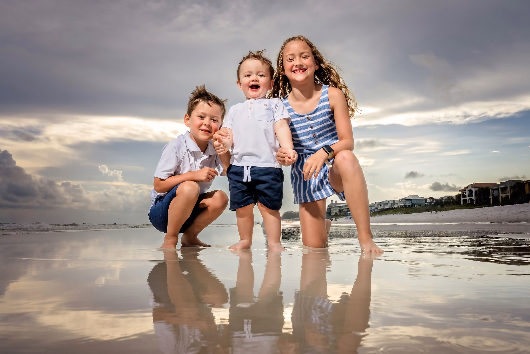 Three children crouched on the reflective sand at sunset