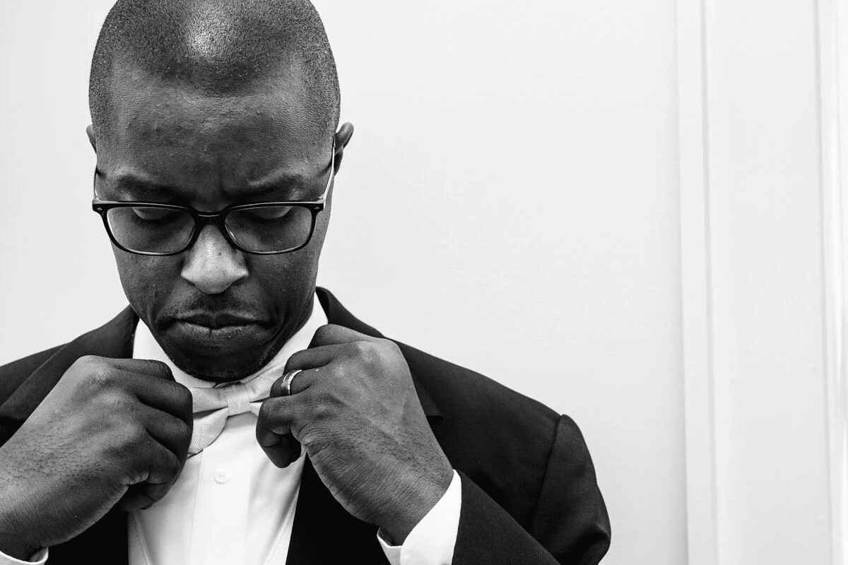 Black-and-white groom fixing his bow tie