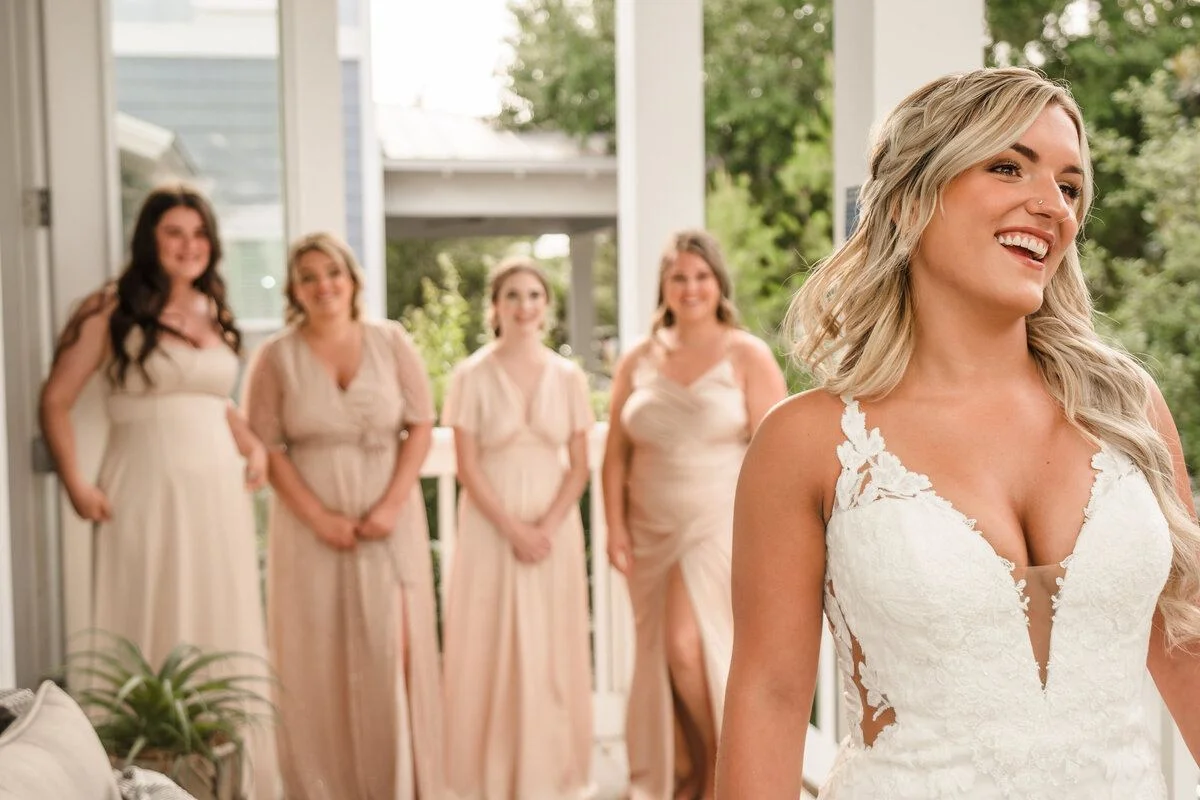 Bridesmaids in blush gowns gather beside the bride on the porch