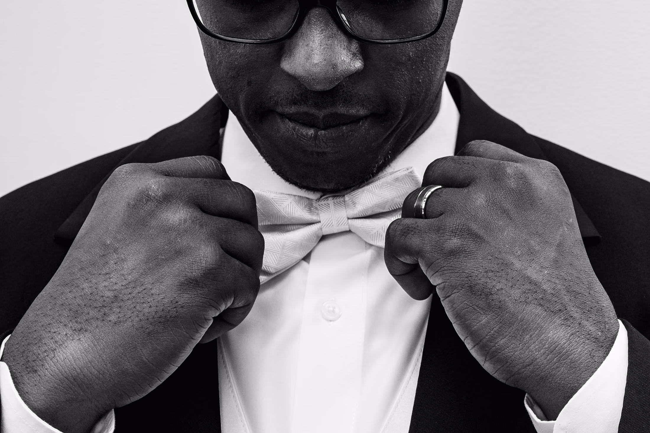 Black-and-white portrait of a groom adjusting his bow tie